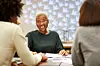 Smiling businesswoman discussing with colleagues at desk. Female entrepreneur is with coworkers at workplace. They are in office.