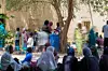 In the street outside the mosque unfolds a scene of everyday community life with several women sitting on the ground chatting while others are handing out food and water.
