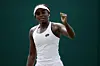 Angella Okutoyi dressed in all-white sportswear raises her fist and smiles during a match, standing against a dark green background.