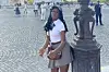 Goll standing in front of l’arc de triomphe in Paris, wearing a white shirt and gray mini skirt.