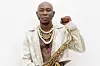 Nigerian Afrobeat musician Seun Kuti looks directly at the camera as he poses with a saxophone in hand, raising a fist with his other hand.