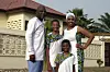 A family of four posing in front of a house wearing outfits designed with white fabrics and African prints.