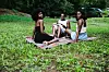 Three young African women sit on the grass. One is reading a book.