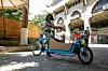 A woman sits on the seat of a long bike in an open marketplace.