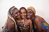 A photo of three women wearing African prints with the rainbow flag.