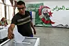 A voter casting ballot at Algerian polling station with a national flag mural in background.