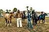 Burna Boy and Shaboozey stand in a ranch setting, in front of horses.