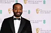 An image of the actor Chiwetel Ejiofor in a tux smiling at the camera on the red carpet of the British Academy Film Awards show.