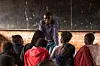 Charles Lipanda stands at the front of a classroom, speaking to a group of young students seated before him at Dzaleka Refugee Camp.