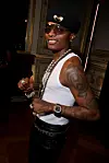 Wizkid poses for a photo wearing a white tank shirt, black leather pants, black beret, and a bright smile.