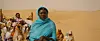 A still image from the film of a woman in the desert in a full headscarf looking pensive.