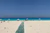 People on a beach on Egypt’s North Coast, dotted by white umbrellas in front of a turquoise blue sea.