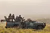 Six people with long-lens cameras in a large jeep, filming the nature and wildlife around them, all smiling. The jeep has an ‘Africa Refocused’ sign.