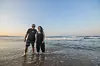 Noel Kok and Pragna Parsotam-Kok standing in the water on a beach, smiling into the camera. Kok is wearing a black 'Africa Refocused' t-shirt.