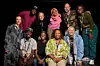 A group of people of different ages and genders take a group photo in a black studio, smiling into the camera.