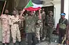 Sudanese army soldiers posing for a picture in the presidential palace in Khartoum. A man in acamouflage T-shirt is standing in front, waving the a Sudanese flag.