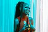 Njerae, a Kenyan singer, laughs while leaning against a curtain.