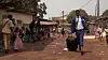 A still from the film of a barefoot Thierno Souleymane Diallo walking through Guinea with a suitcase.
