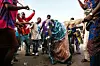 An image of a group of men at Nigeria's Egungun Festival, with sticks circling another man who is wearing colorful regalia and dressed up as an ancestor.