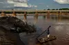 A photo of a man paddling a boat across the Lucite River after the bridge was damaged during Cyclone Idai, on March 26, 2019, outside of Magaro, Mozambique.
