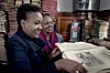 Angela Wachuka and Shiro Koinange review historical documents in the Macmillan Memorial Library, surrounded by old books.