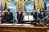 U.S. President Donald Trump stilling behind desk in Oval Office holds up the peace deal bearing his signature while Olivier Nduhungirehe, Rwanda's foreign minister, US Vice President JD Vance, Marco Rubio, US Secretary of State, and Therese Kayikwamba Wagner, Democratic Republic of the Congo foreign minister, are standing and look on.