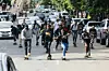 A group of skateboarders ride down a city street in Nairobi, surrounded by traffic and onlookers, capturing the energy and unity of the local skateboarding scene.