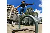 George Zuko is in mid-air while jumping over a metal rail on a sidewalk.