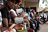 A group of young Namibians seated in a line, holding up their voter registration cards.