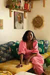 Samiat Salami wears a pink grown and sits on a long couch decorated with African prints.