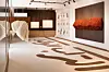 A white and brown art gallery with white and orange textiles on display. Brown Arabic calligraphy is written on the floor.