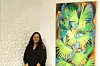 Hadia Temli standing next to a blue and green painting of plants by Rachid Bouhamidi.
