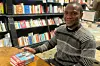 A photo of Chukwuebuka Ibeh sitting in a library with three copies of his book “Blessings” on the table.