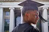 Philip in profile in black graduation cap and gown, with pillars of MIT building in the background.