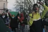 Community organizer Mohamed Koubbani speaks into a microphone at a protest in London, wearing silver sunglasses and a light green and black jacket. Behind him, a man is holding up a Sudanese flag.