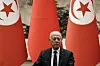Tunisian president sitting in front of two large red flags adorned with Tunisia's national emblem.