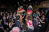 Two people are dancing in the middle of a crowded dance floor in human-sized dinosaur suits