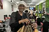 A photo of Nikiama Kisun Sira Fatimata in her salon braiding a client’s hair, and wearing a black blouse with white Polka Dot sleeves.