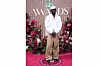 Black Sherif poses in front of a floral backdrop wearing a loose-fitting shirt and baggy pants on the 2025 BET Red Carpet.