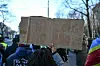 Protest sign reading 'NO CONGO NO PHONE' held by a demonstrator during a street protest, with other protesters and trees visible in the background.