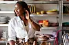 Person in white shirt arranging hair, standing by shelves of colorful dinnerware.