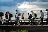 Many young men with backpacks walking on or sitting by a metal barge, some are blurry and some are in focus. Most are wearing slippers.