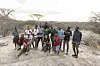 A group of people holding cameras are posing for a photo, standing on a rock plateau in nature with green landscapes behind them.