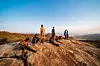 Nine boys carve bows and arrows on a plateau. Behind them is Tanzania's vast natural landscape of trees and lakes.
