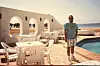 Ahmed Adel Wahby is standing by the pool in his Bawaki Beach Resort, wearing striped white and blue shorts and a blue t-shirt. Behind him is a white arc, around him white plastic tables with chairs, and in the distance, the Red Sea.