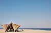 People sitting in the shade of a straw hut built at a Red Sea beach with yellow sands and multi-colored blue water.