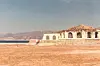 A white structure with large, arc-shaped windows on a Red Sea beach. The sea and the mountains are in the background.