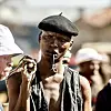 Warren Masemola wearing a black beret with a pipe in his mouth stares intensely at another character from 'Tjovitjo.'