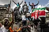 Kenya protestors holding up flags and the middle finger, climb a statue in the city center during demonstrations.