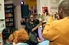 Justine Wanda smiling and holding a bouquet while audience members applaud at a comedy event in a bookstore.